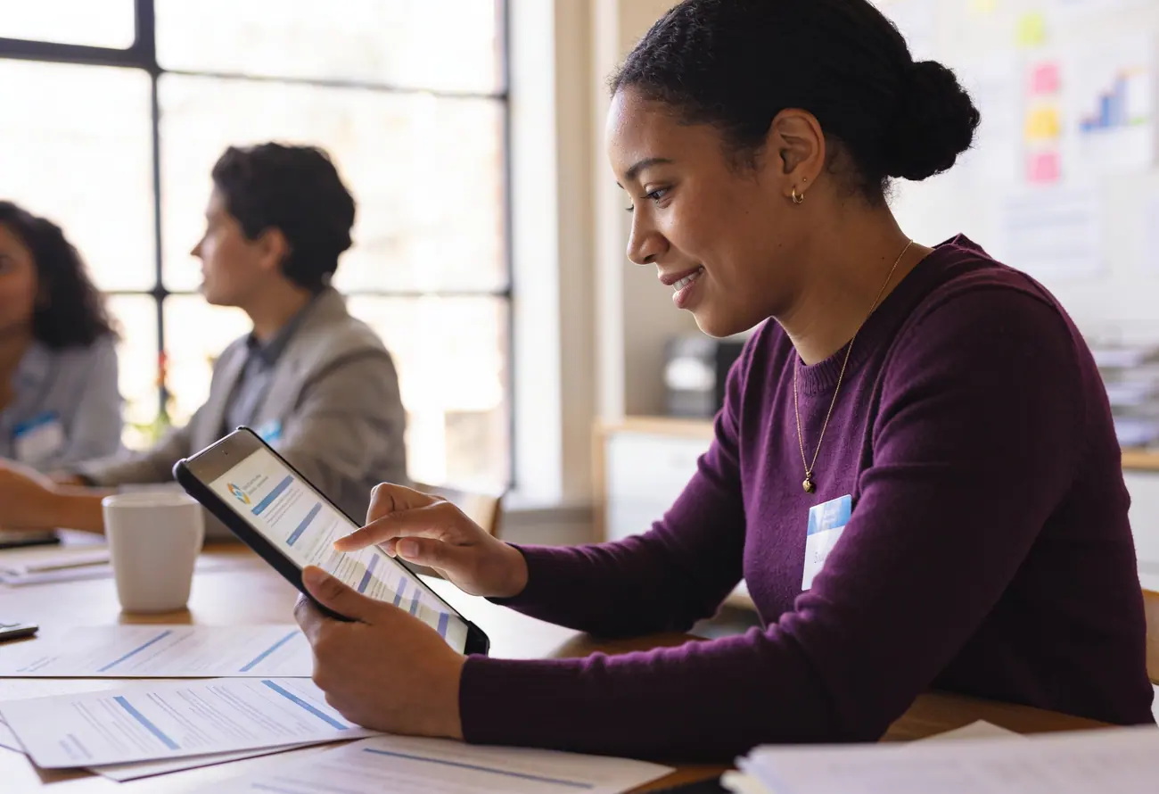 An organiser going through a printed budget on a tablet at a meeting table